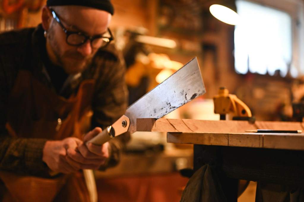 Carpenter sawing wood in workshop with hand saw
