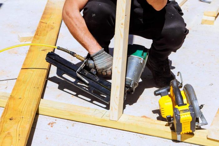 Construction worker uses nail gun to secure wooden frame during building works at construction site