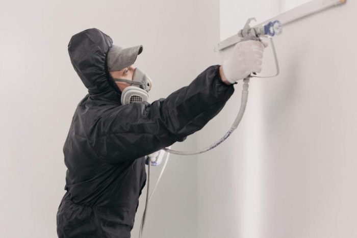 Decorator painting wall with spray indoors