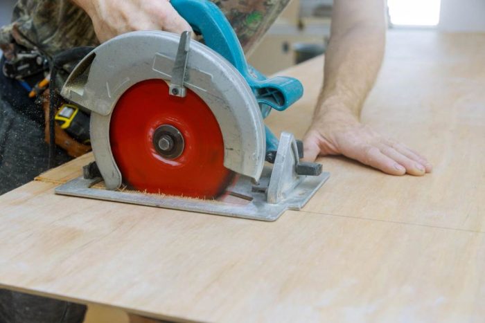 Man using a circular saw to cut plywood at woodwork production factory