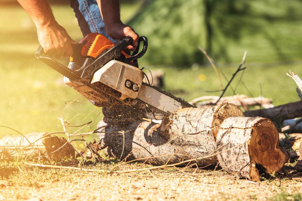 Person safely operating a gas powered chainsaw with full protective gear