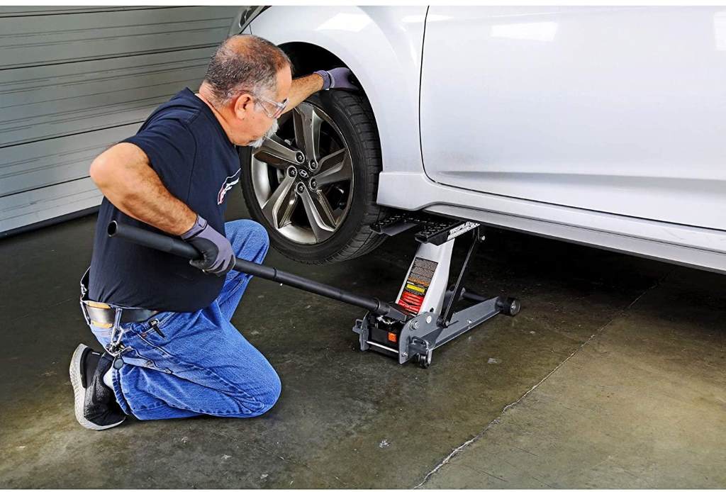 Person safely using a car jack to lift a vehicle on a flat driveway