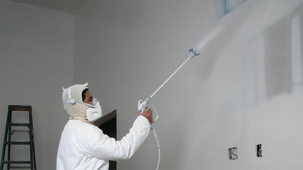Person using a paint sprayer to achieve a smooth wall finish indoors