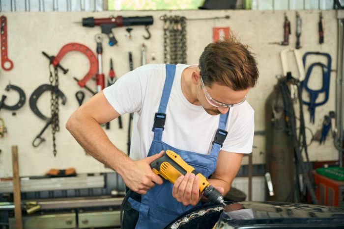Service station master auto mechanic tightens bolts of inside of car with drill